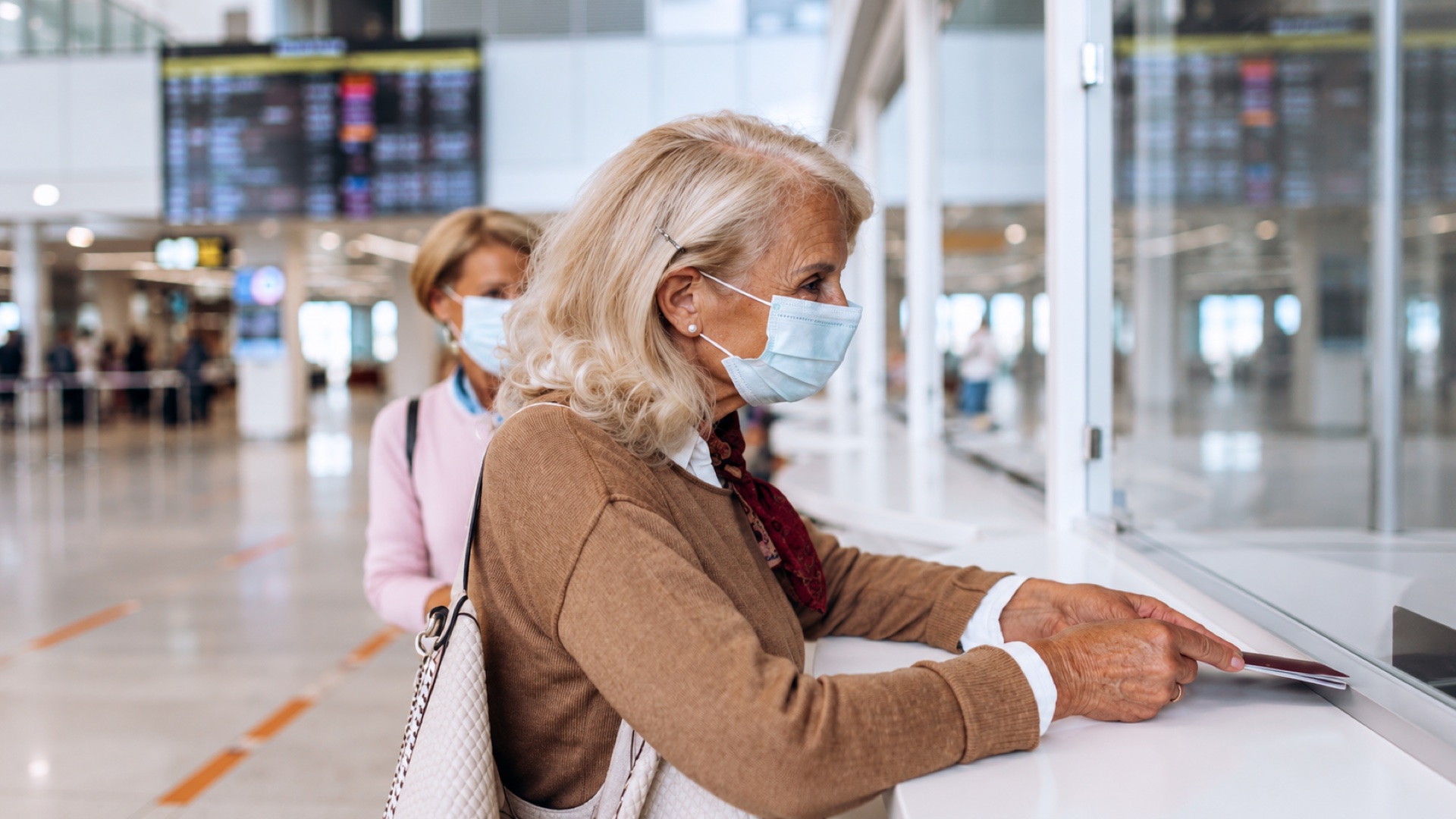 Passageira idosa de máscara apresenta seus documentos no balcão de atendimento do aeroporto.