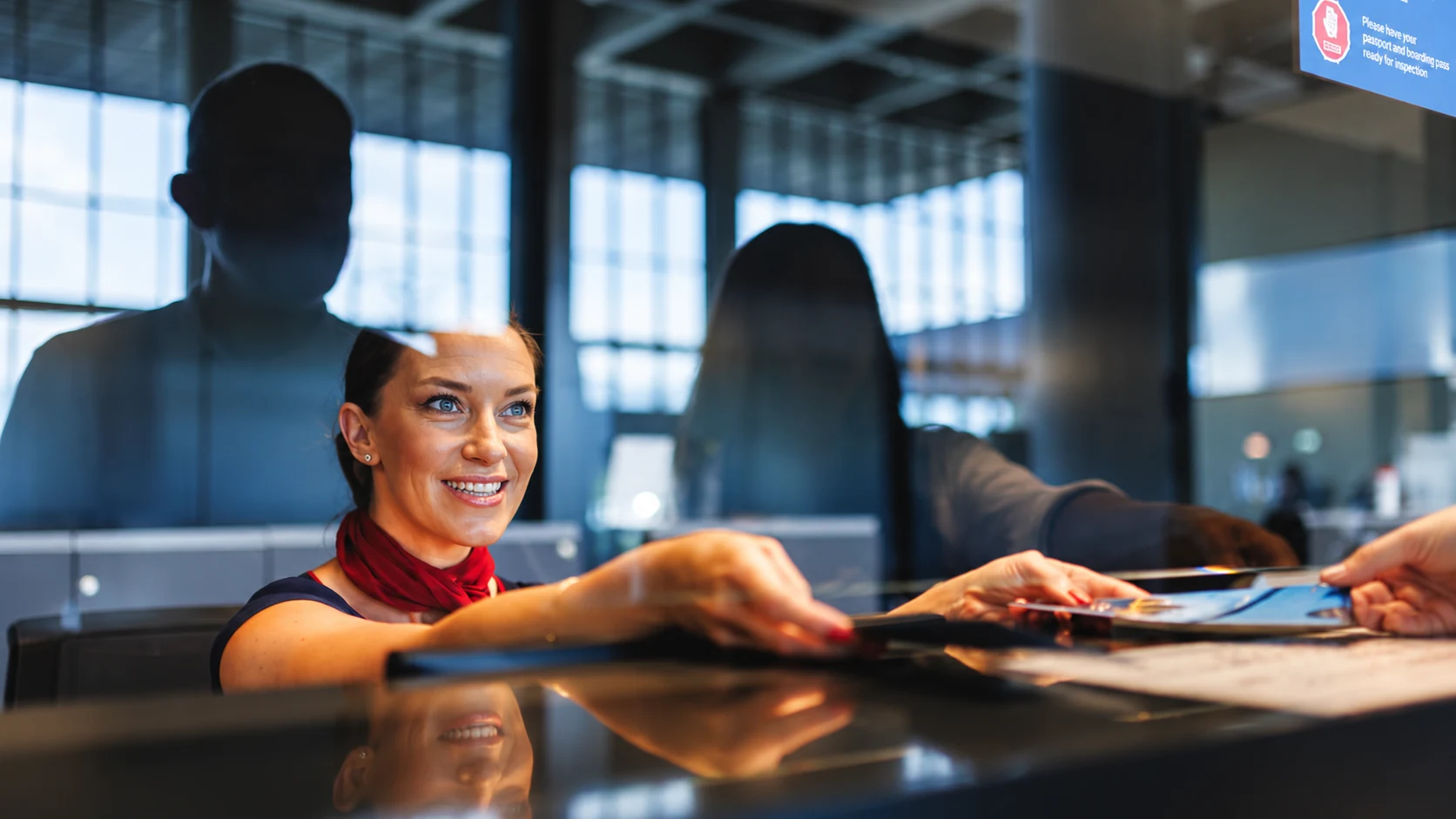 Profissional do aeroporto recebe uma passageira com um sorriso no check-in.