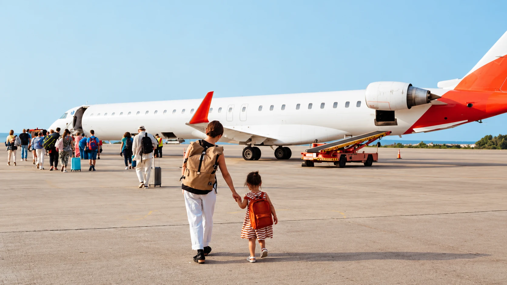 Adulta e criança caminham de mãos dadas em direção ao avião em um dia ensolarado.