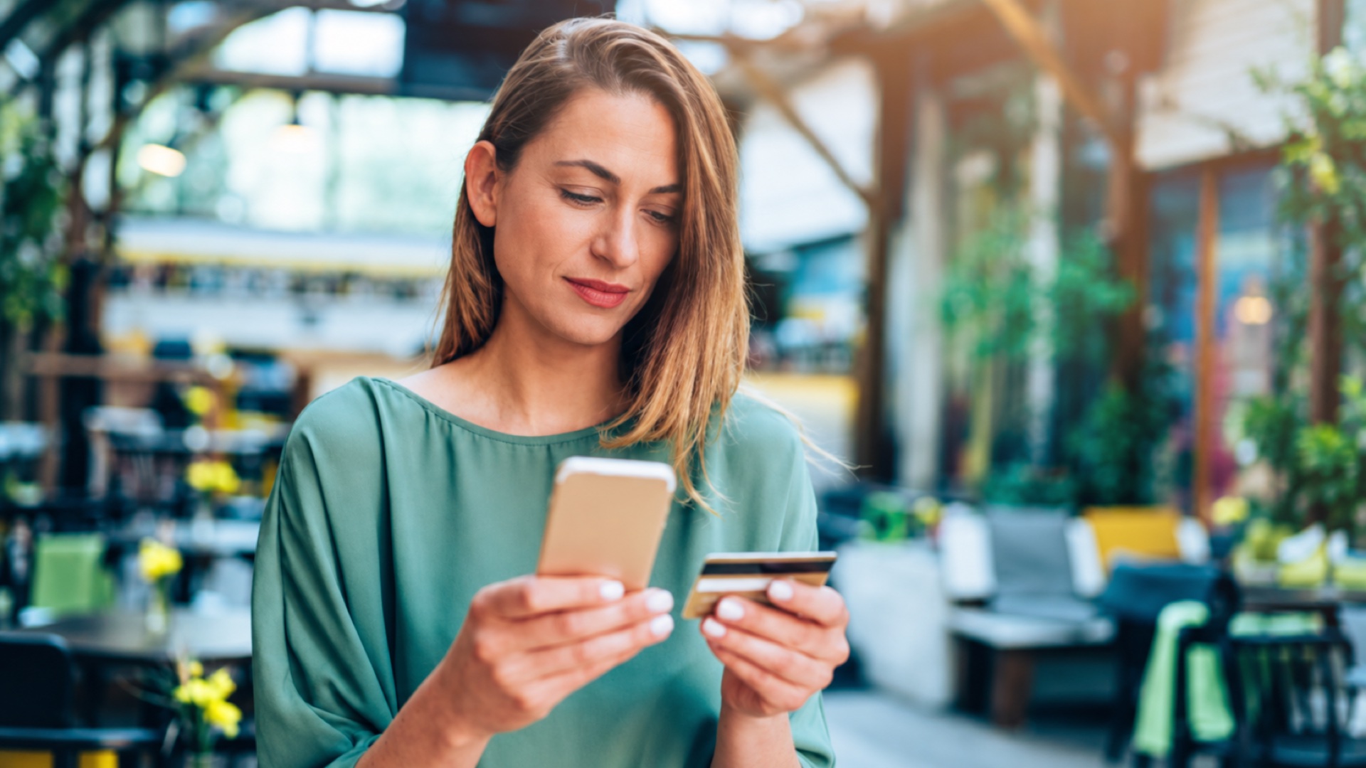 Mulher confere o celular com expressão concentrada enquanto segura um cartão de crédito.