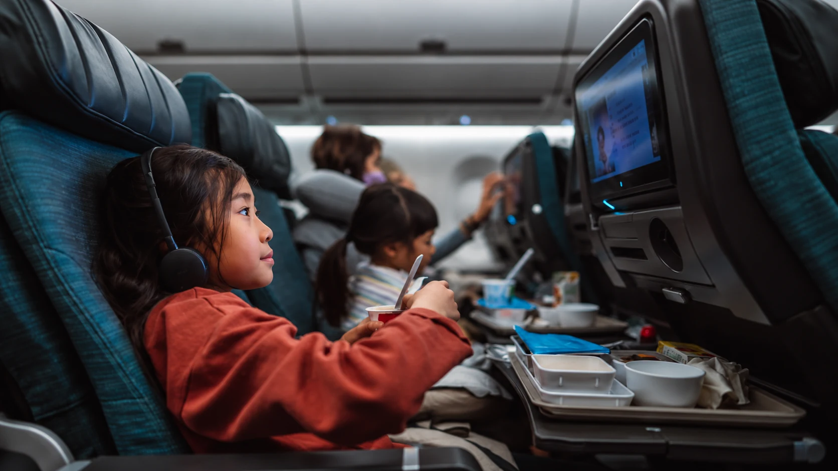 Criança faz uma refeição a bordo enquanto assiste à tela do avião.